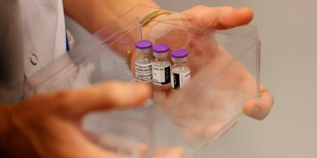 Eine medizinische Fachkraft hält einen transparenten Behälter mit lediglich 3 Impfdosen in den Händen