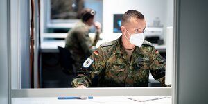 Ein Bundeswehrsoldat mit Mundnasenschutz schaut auf einen Computerbildschirm