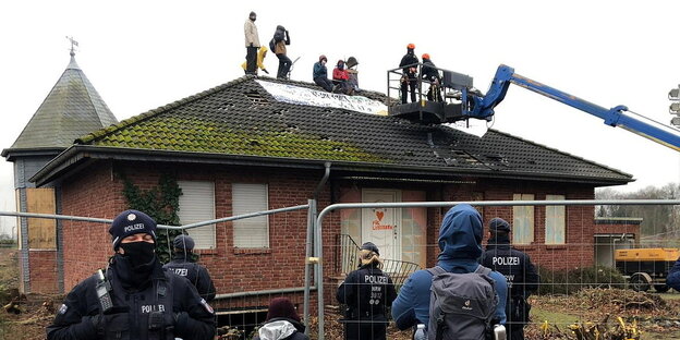Aktivisten sitzten auf dem besetzten Hausdach, im Vordergrund stehen Polizisten