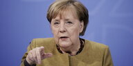 Angela Merkel sitzt vor einem blauen Hintergrund und gestikuliert