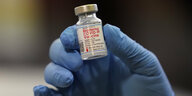 Eine blau behandschuhte Hand hält eine Impfdosis des Moderna-Vakzins