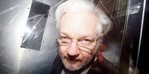 Julian Assange, ein älterer Mann mit weißen Haaren und Brille.