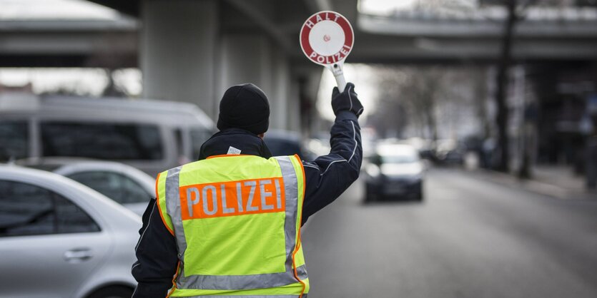 Ein Polizeibeamter stoppt ein Auto mit Hilfe einer Polizeikelle im Rahmen einer Verkehrskontrolle