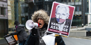 Eine Demonstrantin hält ein Plakat mit eimnem Bild von Julian Assange und der Aufschrifft "Hands off Assange" hoch und ruft durch ein Megafon