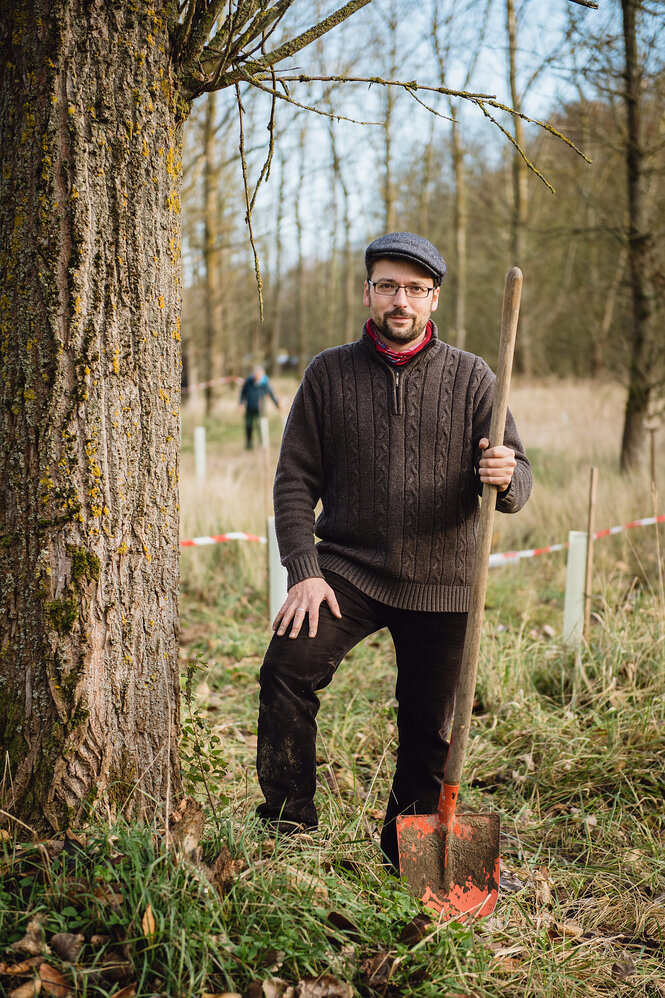 Karl Grünberg steht mit einer Schaufel neben einem Baum