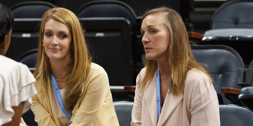 Zwei Frauen sitzen auf Plastiksitzen in einem Basketballstadion