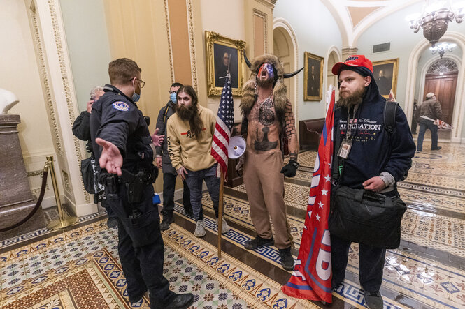 Mit Hörnern und Fell beklediet schreit ein Tätowierter Trumpunterstützer gegen die Polizisten an