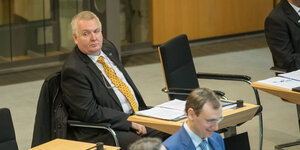Ein älterer weiße Mann sitzt an einem Pult im Berliner Abgeordnetenhaus. Er trägt Anzug, Krawatte und eine Anstecknadel der AfD