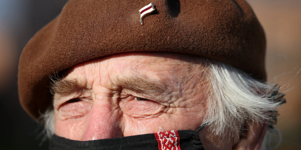 An der braunen Baskenmütze eines äteren Herren hängt eine kleine belerussische Flagge als Anstecker - der Mand trägt Mund-Nasenshutz