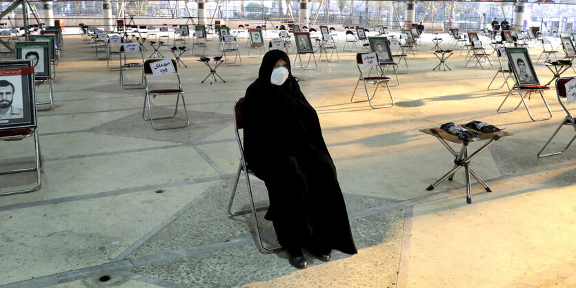 Eine Frau in Vollverschleirung sitzt in einer Halle auf einem Stuhl