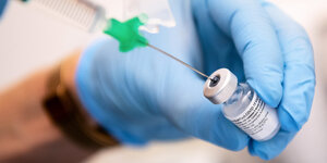 Behandschuhte Hand zieht eine Spritze mit dem Impfstoff auf