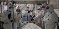 Eine Gruppe von medizinischem Personal steht in weißen Schutzanzügen um ein Krankenbett