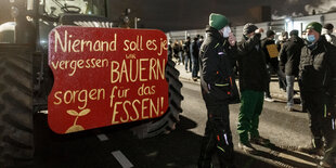 Bauer mit Plakat "Niemand soll es je vergessen, wir Bauern sorgen für das Essen" und eine Gruppe Bauern im Dunkeln vor einer Molkerei