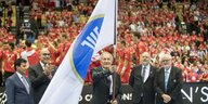 Handballpräsident Hassan Moustafa mit Fahne im Vordergrund, dahinter Handballspieler und Publikum