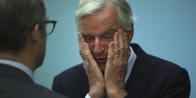 Michel Barnier stützt das Gesicht mit den Händen und hat die Stirn gerunzelt.