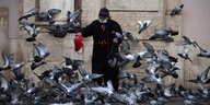 Eine Frau mit Maske füttert Tauben, die wild auffliegen