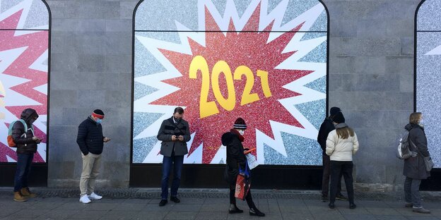 Menschen vor einem Schaufenster mit großem Schriftzug "2021" se´tehen in Abstand zueinander