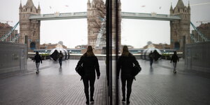Frau läuft Richtung Tower Bridge in London und spiegelt sich in einem Fenster