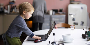 Ein Kleinkind spielt in der Küche am Laptop seiner Mutter