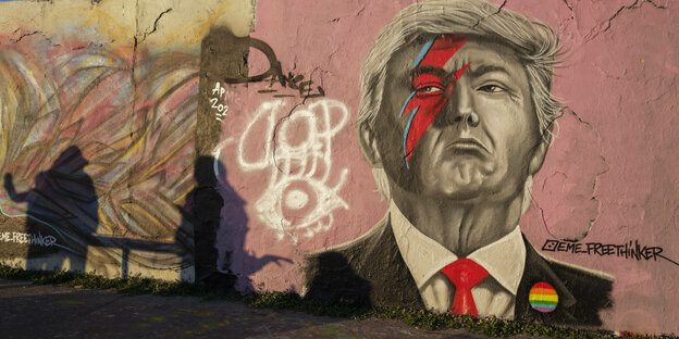 Graffiti-Wand in Berlin zeigt schlecht gelaunten Donald Trump mit david bowie blitz und Regenbogenabzeichen