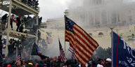 Menschen auf Baugerüst und mit USA-Flaggen vor verrauchtem Kapitol