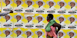 Eine Frau läuft vor Wahlplakaten auf denen Yoweri Museveni zu sehen ist