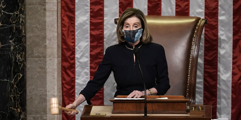 Nancy Pelosi mit einem Hammer in der Hand vor US-Flagge.