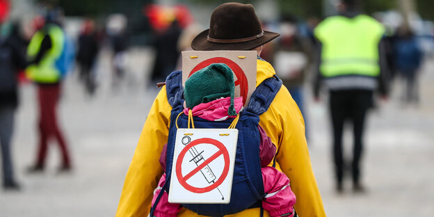Eine Demonstrantin mit einem Schild gegen Impfungen auf ihrem Rücken (durchgestrichene Spritze)