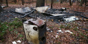 Verbrannte Reste des Baumhauses und ein Holzofen liegen auf dem Waldboden