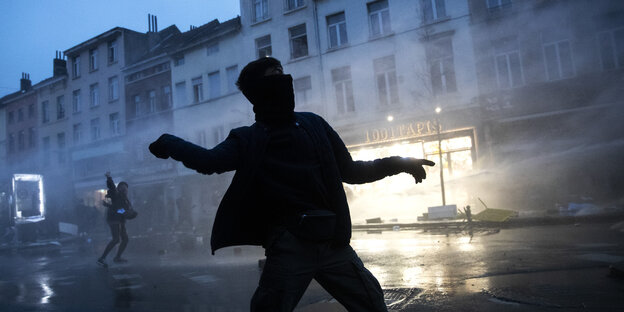Ein Demonstrant wirft Steine in Richtung von Polizeibeamten