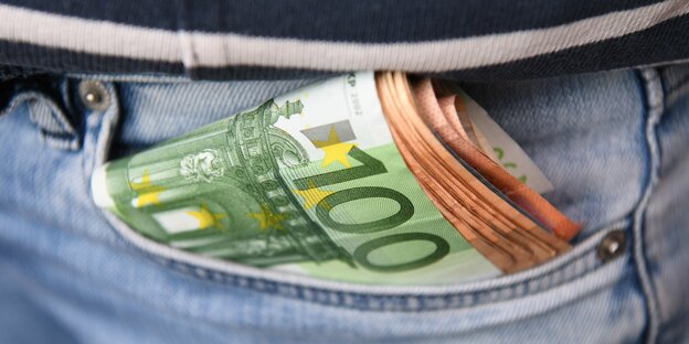 Geldscheinbündel luggt aus einer hinteren Jeanshosentasche hervor Geldscheinbündel luggt aus einer hinteren Jeanshosentasche hervor