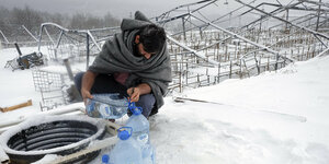 Ein Geflüchteter füllt im verschneiten und abgebrannten Lager in Lipa an einem Brunnen Wasser in Plastikflschen