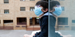 Ein Junge mit Mundschutz sieht aus dem Fenster