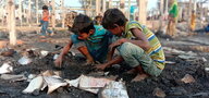 Zwei Kinder graben am Boden in Asche nach Brand im Flüchtlingslager.