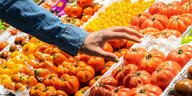 Eine Hand greift nach Tomaten in einem Supermarkt.