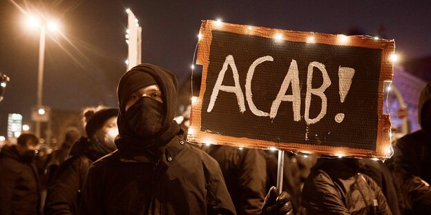 Ein Demonstrant mit einem schild, auf dem ACAB steht.