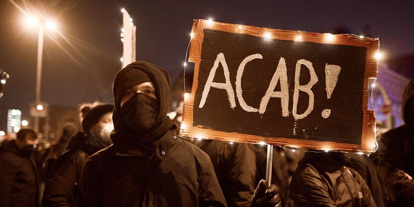 Ein Demonstrant mit einem schild, auf dem ACAB steht.