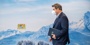 Markus Söder läuft mit Maske an einer blauen Wand vorbei