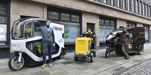 Drei Paketboten mit ihren Lastenrädern vor einer Ziegelfassade