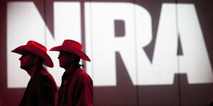 Zwei Männer mit Cowboyhüten vor einem riesigen leuchtenden NRA-Logo