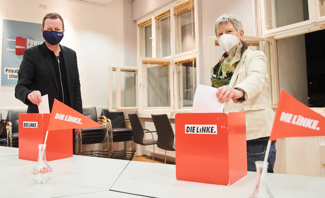 Zwei Menschen werfen Wahlzettel in Urnen