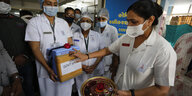 Mediziner hält Box mit Impfstoff, eine Frau drückt einen roten Punkt drauf