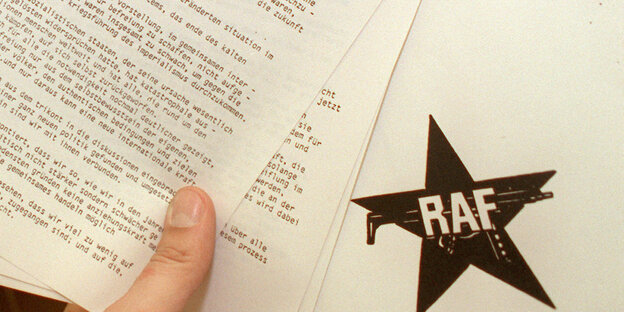 eine Hand hält mehrere Seiten bedrucktes Papier. Darauf ist auch das Logo der RAF zu sehen