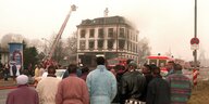 Eine Gruppe schwarzer Männer steht vor einem ausgebrannten Haus