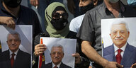 Drei verhüllte Personen halten Plakate von Mahmoud Abbas.