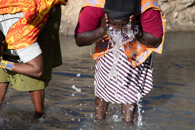 Zwei Frauen stehen mit den Beinen im Flusswasser und waschen ihre Gesichter