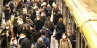 Menschenmenge mit Masken dicht gedrängt,daneben gelbe U-Bahn