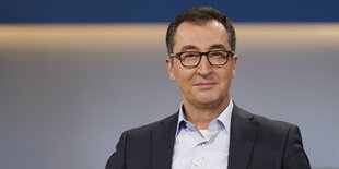 Cem Özdemir lächelt - er ist ein älterer Mann mit kurzem, dunklen Haar und einer großen Brille mit dickem Rand.