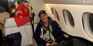 Mesut Özil sitzt im Flugzeug. Im Hintergrund türkische Nationalflagge und Vereinsflaggen von Fenerbahçe