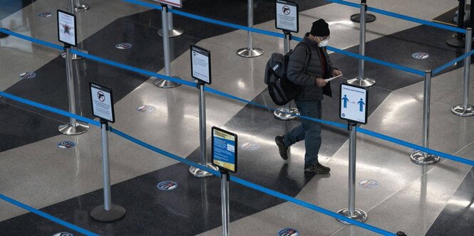 Eine mit Bändern abgesperrte Sicherheitszone im Flughafen. Ein Fluggast mit Maske geht dort entlang